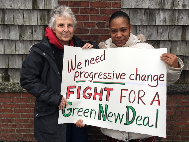 two women holding a sign reading We need progressive change fight for a Green New Deal